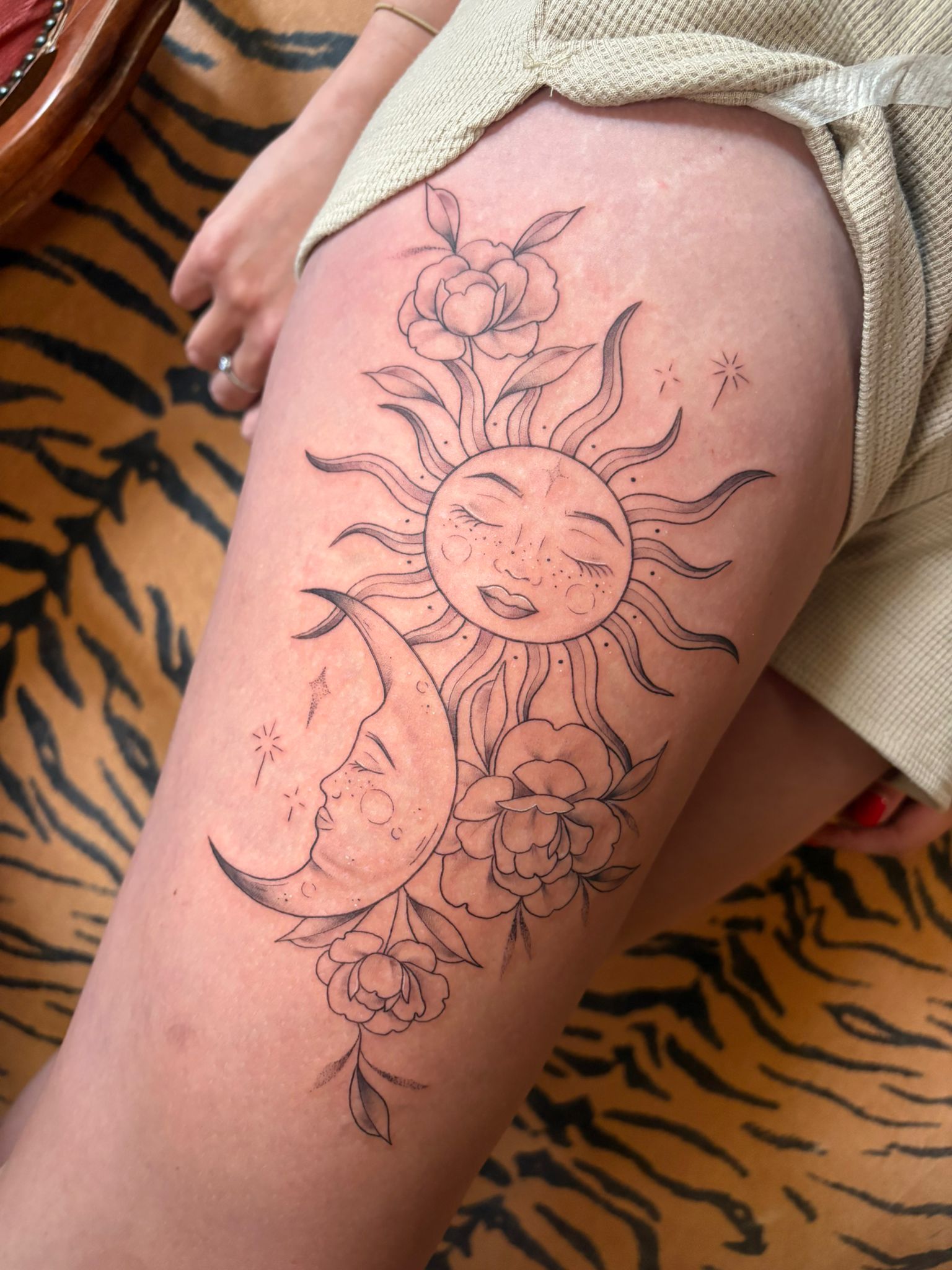 Fine-line sun, moon and floral thigh tattoo by Nicole